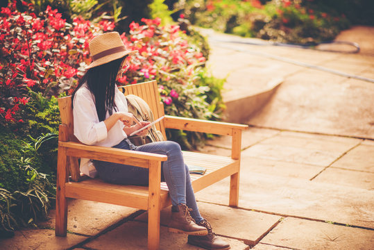 beautiful woman wearing sunglasses and hat sit on wooden chair in flower garden