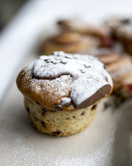A delicious, freshly baked chocolate covered chocolate chip muffin frosted or spinkled with icing sugar on a business breakfast buffet