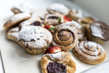 A selection of freshly baked and frosted Danish pastries and sweet buns or muffins on a business breakfast buffet sprinkled with icing sugar and garnished with strawberries