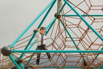Little boy walking barefoot on red ropes while holding to pyramid net structure at playground on...