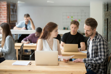 Fototapeta premium Confident female worker explaining company plan to male colleague working on laptop in coworking space. Coworkers exchanging ideas on success strategy analyzing business reports. Concept of teamwork