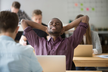 Satisfied black worker leaning back in chair with eyes closed in coworking space. Happy african...