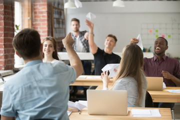 Colleagues having fun launching paper planes in modern coworking office, celebrating company success and win. Diverse work team entertaining on break. Multiethnic group having good time, relaxing