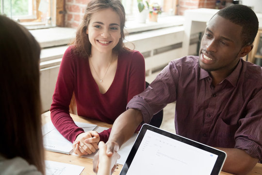 Multiracial Couple Closing Deal With Realtor Buying Home Together, Documenting Mortgage, Taking Loan. African American Husband And Caucasian Wife Making Agreement With Real Estate Agent Purchase House