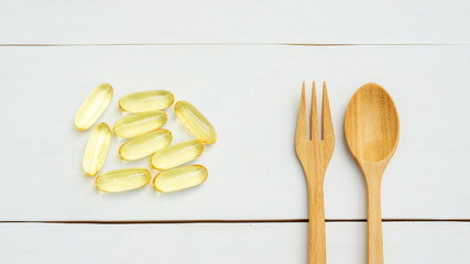 Fish oil, spoon, and fork on a white wooden table.
