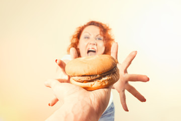 Big woman eat fast food. Red hair fat girl with burger. Unhealthy food concept with plus size female