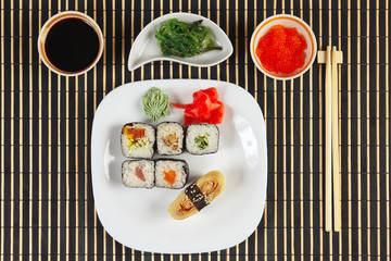 Sushi set, hiyashi wakame salad, soy sauce and salmon caviar on a black bamboo mat. View from above.