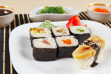 Sushi set, hiyashi wakame salad, soy sauce and salmon caviar on a black bamboo mat close up.