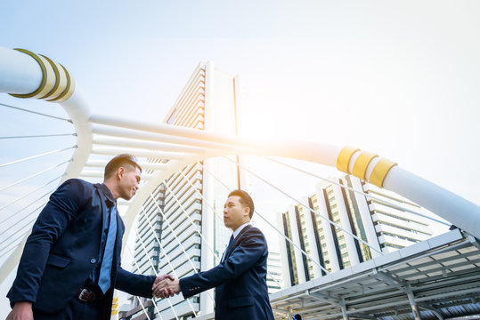 Two asian business have handshake with building and city background.
