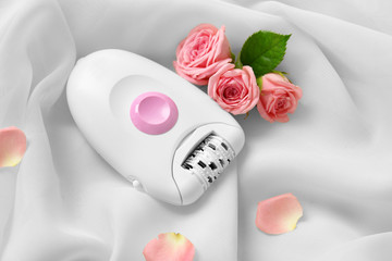 Modern epilator and flowers on light fabric