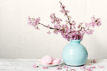 Pink cherry blossom flower bouquet with macarons in blue vintage vase on white wooden background