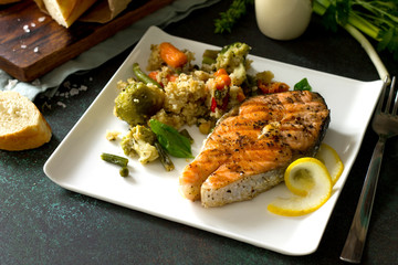 Grilled salmon steak, couscous and vegetables (string beans, brussels sprouts, carrots, sweet peppers, tomatoes) on stone or concrete table. Healthy proper nutrition.