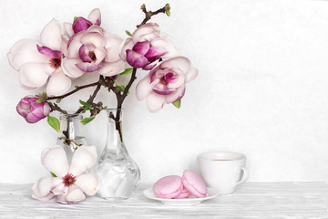 Pink magnolia flowers bouquet with coffee cup and macarons on white wooden background