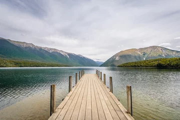 Foto op Plexiglas Lake Rotoiti, Tasman, Nelson Lakes, New Zealand: Beautiful scenic view to great mountain range lake with wooden jetty pier and pretty smooth reflections on the water surface at a cloudy rainy day © Thomas Jastram