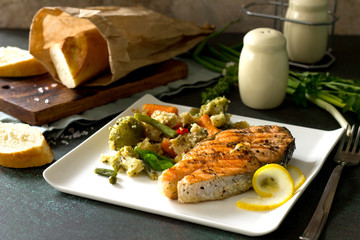 Grilled salmon steak, couscous and vegetables (string beans, brussels sprouts, carrots, sweet peppers, tomatoes) on stone or concrete table. Healthy proper nutrition.