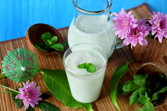 Coconut milkshake with mint flavour in a glass surrounded by coconut shells and pink flowers