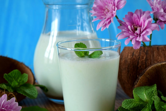 Coconut milkshake with mint flavour in a glass surrounded by coconut shells and pink flowers