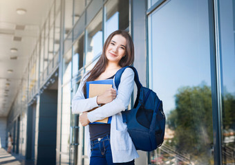 Young female IT student, with books and backpack. Staying outside before lesson and smiling