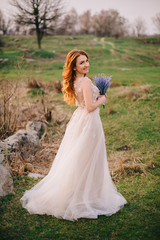 Fototapeta na wymiar young red-haired woman standing with flowers in hands and smiling against the background of nature, spring