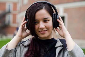 Headshot of young asian girl with headphones listening to the music and dancing at the street
