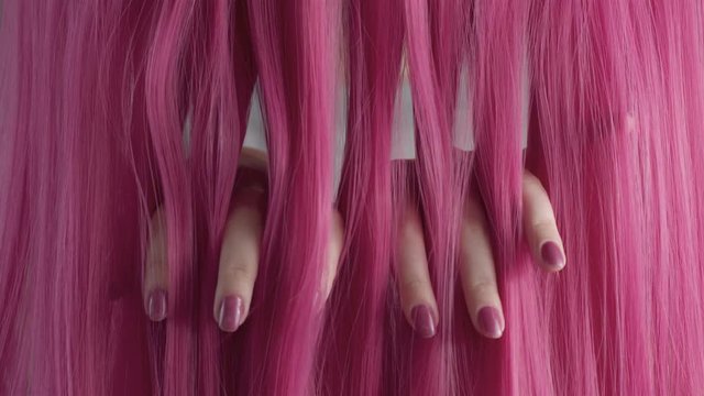 Closeup of pink hair creative colored texture woman's hand with pinc manicure through pink hair texture