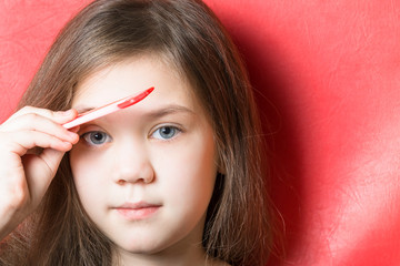 Cute little girl combs her eyebrows with a comb on a red background