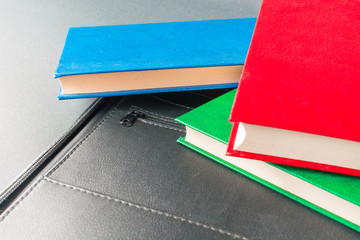 Stack of colorful books lies on a black leather folder