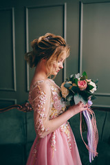 portrait of a young woman in a pink dress holding a bouquet in her hands against a vintage interior background