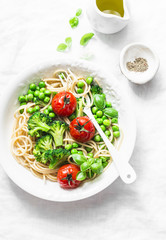 Simple veggie pasta. Vegetarian pasta spaghetti with broccoli cabbage, green peas and cherry tomatoes on light background, top view