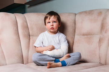 a small boy is sitting on a chair with a broken arm, in a cast. hospital. medicine. danger. pain. to break limbs. violence.