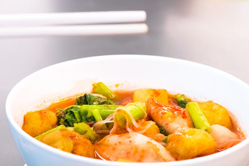 Thai food.Hold chopsticks to meat ball.Pink seafood flat noodles.Spicy lemongrass flavored soup with pork, chicken on white background.Close up