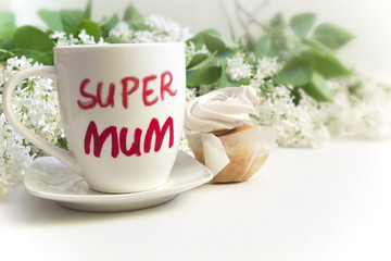 Mother's day concept. Mug with inscription 'Super mum', cupcake and lilac flowers.