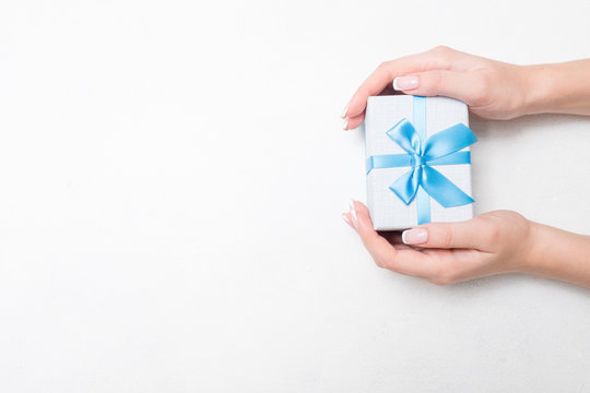 Small Present With Blue Ribbon Bow In Woman Hands On White Background. Sweet Reward Gift For Holiday Or Birthday. Free Space Concept