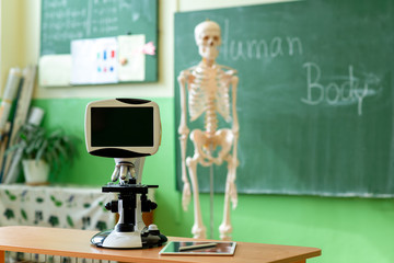 Biology classroom. Artificial human body skeleton, student desk with microskope and digital tablet. Anatomy teaching aid. Education and generation z concept.