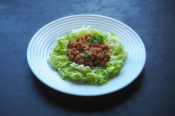 Plate of zucchini spaghetti with beef bolognese on black background.