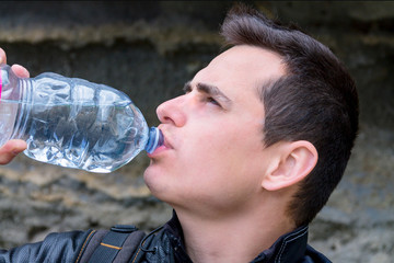 a young guy drinks water from a plastic bottle, a man quenches his thirst