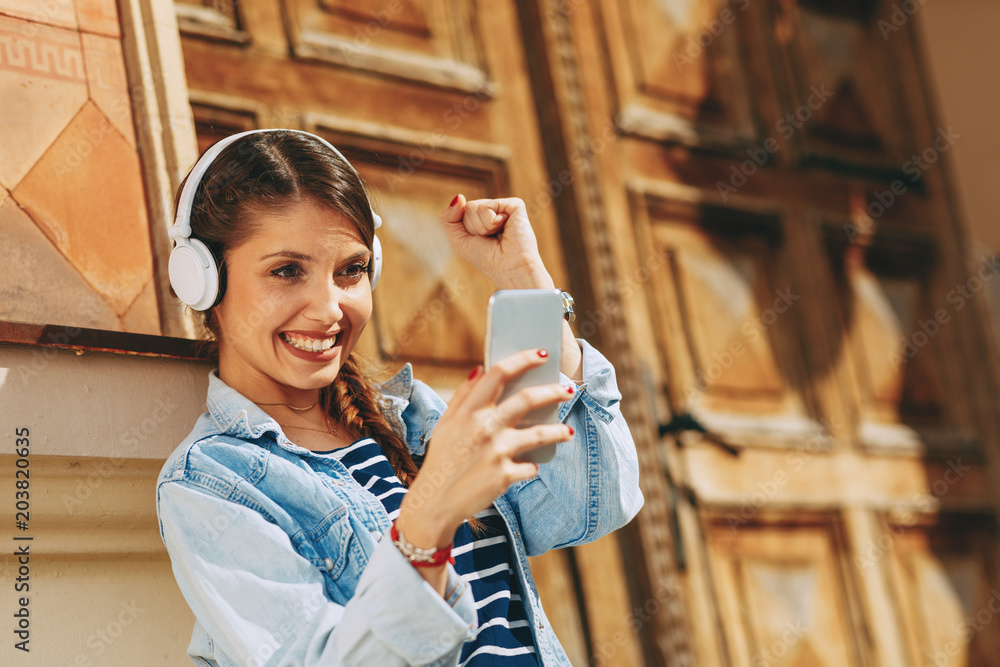 Wall mural Young woman making video call via smartphone and headphones  in the city