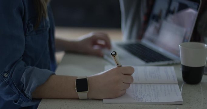 Female Friends talking while working on laptop and writting in notebook