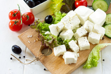 Feta cheese and black olives, cooking qreek salad with fresh vegetables on a white wooden table.