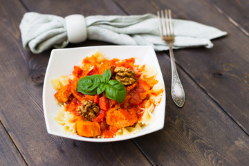Italian pasta - butterfly macaroni (bows) of Farfarello with tomato sauce on a white plate and on a dark wooden background.