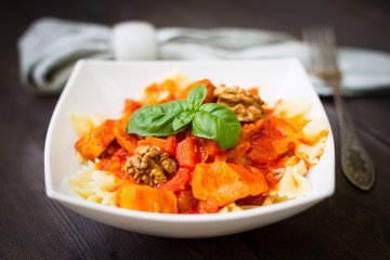 Italian pasta - butterfly macaroni (bows) of Farfarello with tomato sauce on a white plate and on a dark wooden background.