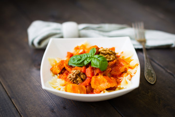Italian pasta - butterfly macaroni (bows) of Farfarello with tomato sauce on a white plate and on a dark wooden background.