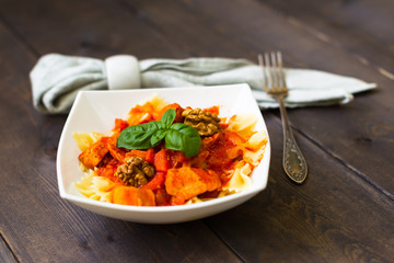 Italian pasta - butterfly macaroni (bows) of Farfarello with tomato sauce on a white plate and on a dark wooden background.