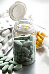Pills in a glass container and other medicines in the background