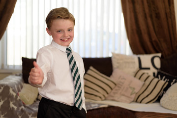 Young boy dressed in new uniform and ready for school, whilst holding thumb up