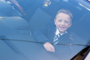 Happy schoolboy looking through car window, ready to go back to school
