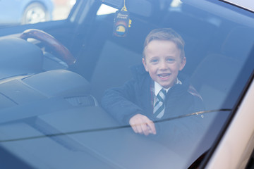 Happy schoolboy looking through car window, ready to go back to school