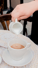 Young caucasian woman pouring milk into morning coffee during breakfast.