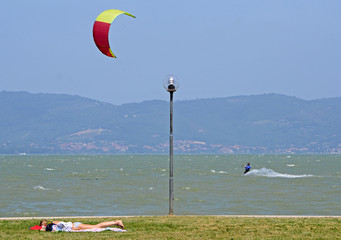 Umbria, Italy, landscape of a windy Trasimeno lake. A man has fun with kitesurfing while a girl is sunbathing