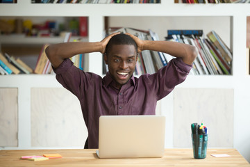 Excited African American worker looking eyes wide open winning lottery online, not believing his...